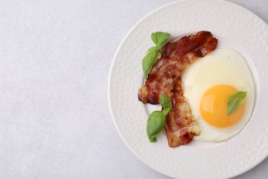 Fried egg, bacon and basil on light grey table, top view. Space for text