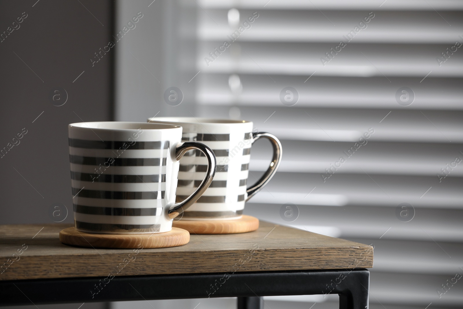 Photo of Mugs of drink with stylish cup coasters on wooden table in room. Space for text