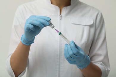 Doctor filling syringe with hepatitis vaccine from glass vial on grey background, closeup