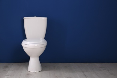 Photo of New toilet bowl near color wall indoors. Space for text