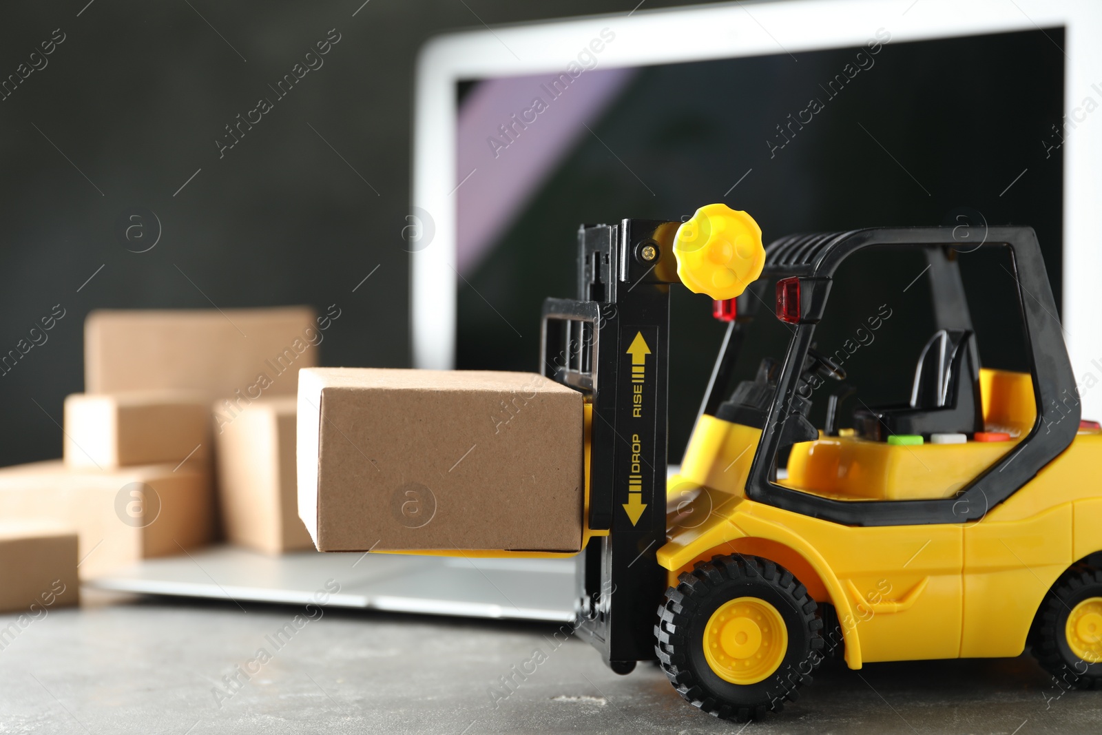 Photo of Toy forklift with box near laptop on table. Logistics and wholesale concept