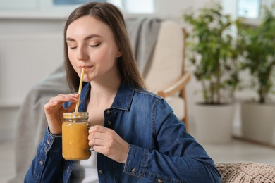 Photo of Beautiful young woman drinking delicious smoothie at home