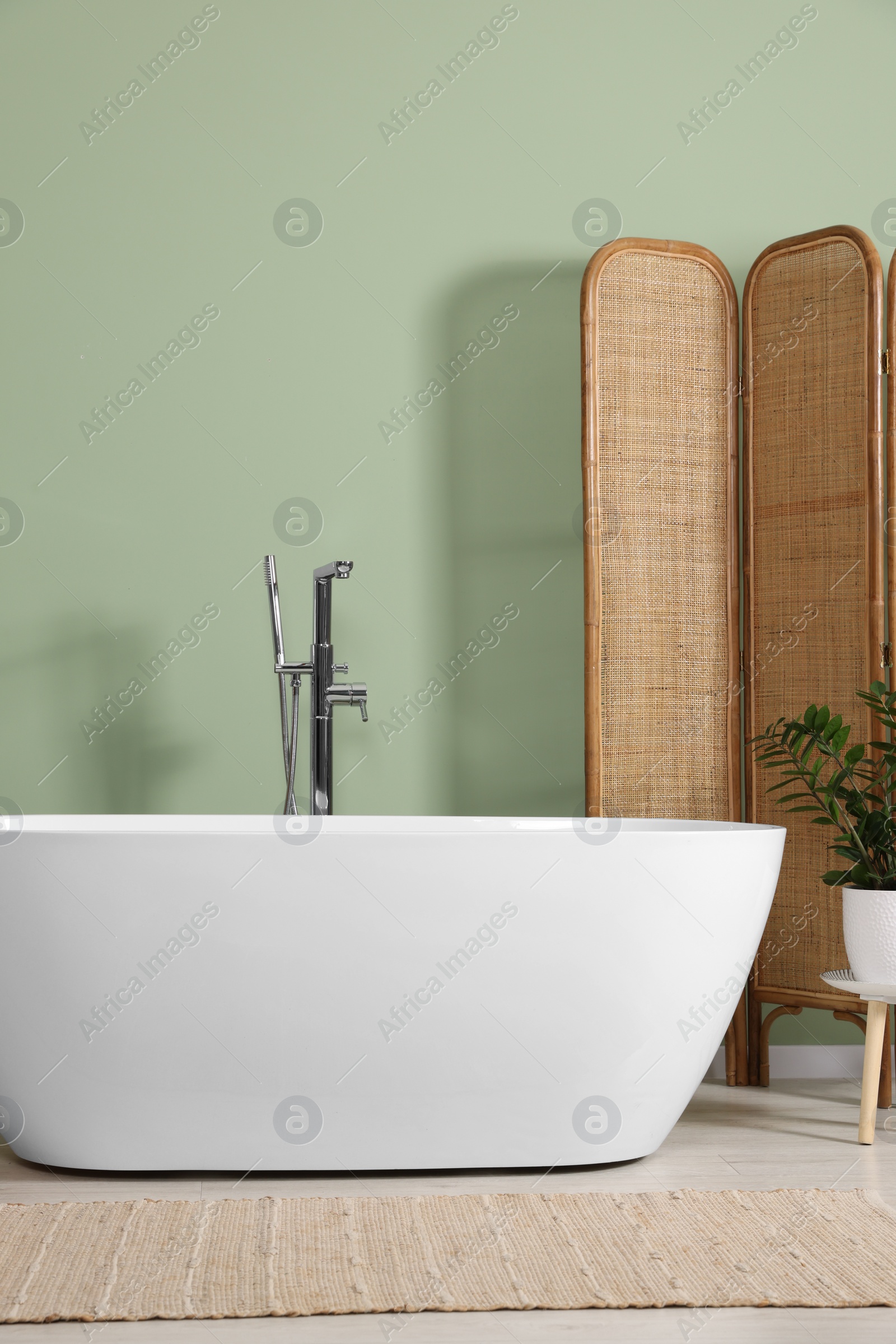 Photo of Modern ceramic tub and beautiful plant near light green wall in bathroom. Interior design