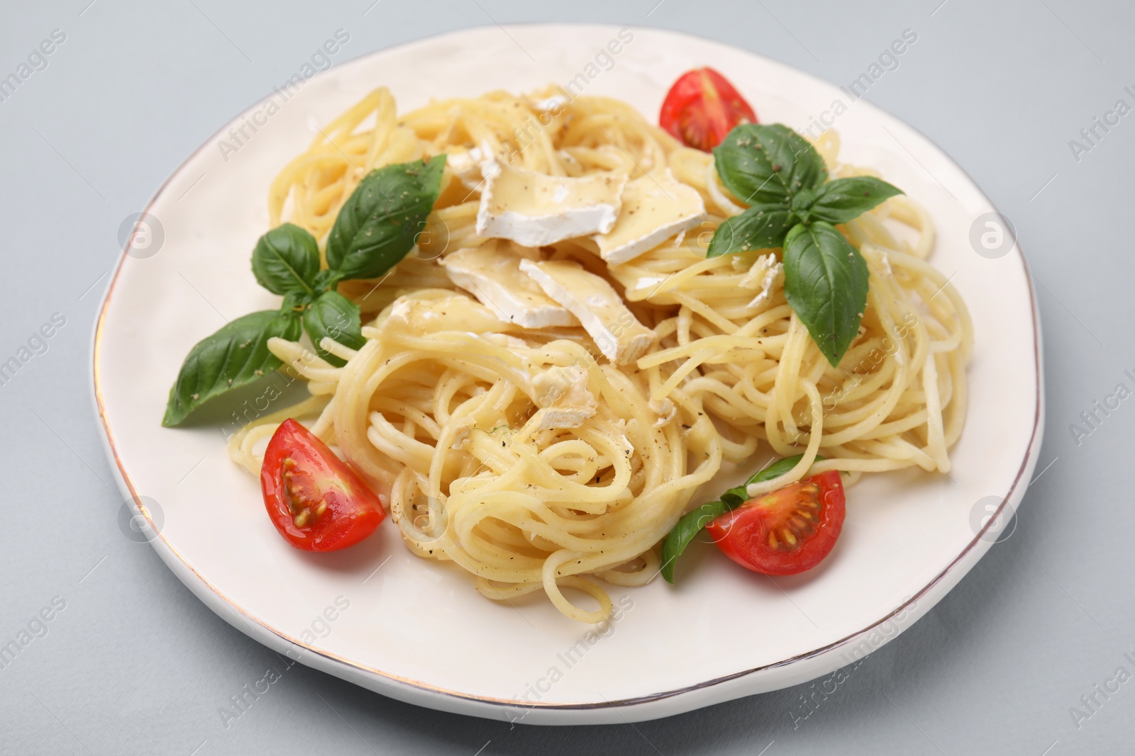 Photo of Delicious pasta with brie cheese, tomatoes and basil leaves on grey background, closeup