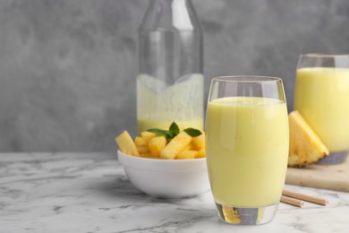 Photo of Tasty pineapple smoothie and sliced fruit on white marble table, space for text