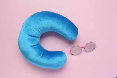 Photo of Light blue travel pillow and sunglasses on pink background, flat lay