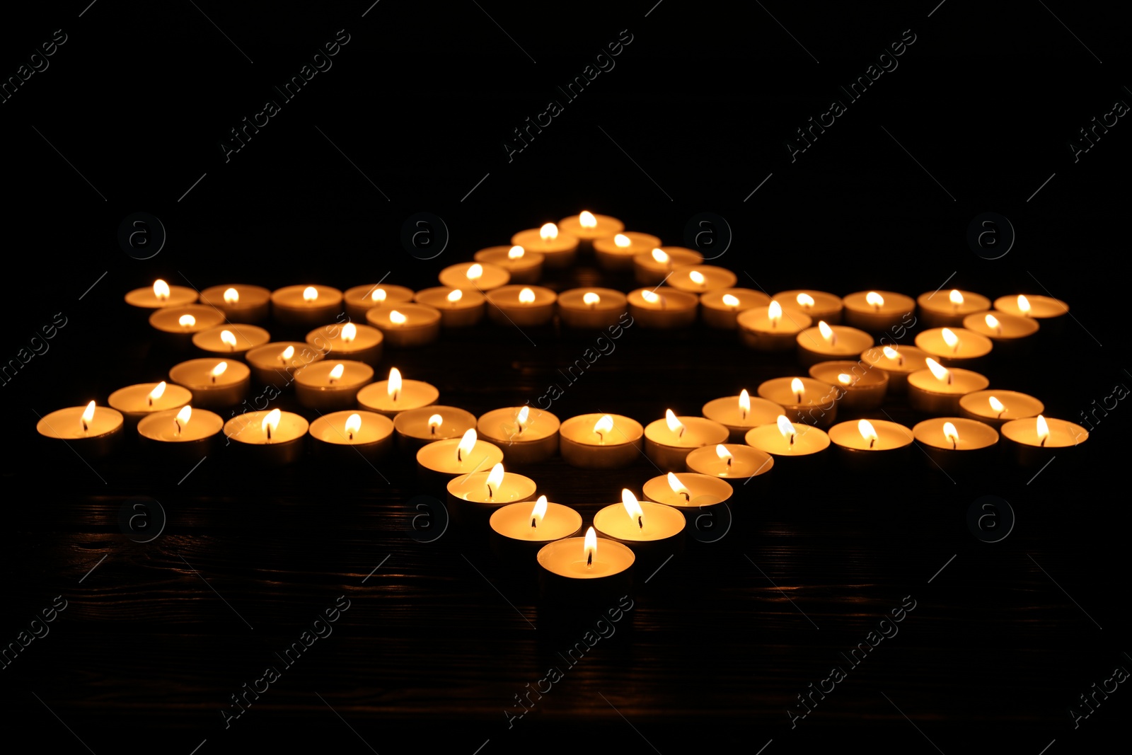 Photo of Star of David made with burning candles on black background. Memory day
