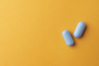 Photo of Pills and space for text on orange background, top view. Potency problem