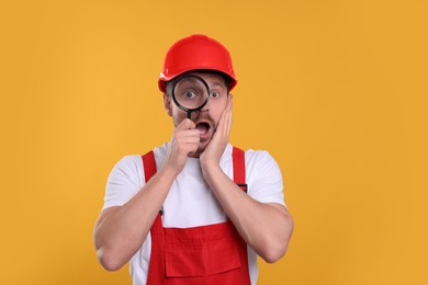 Photo of Surprised builder looking through magnifier glass on yellow background