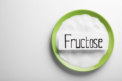 Bowl of sugar and paper sheet with word Fructose on white background, top view. Space for text