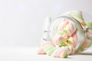 Photo of Glass jar with colorful marshmallows on white table against blurred lights, closeup. Space for text