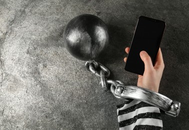 Photo of Prisoner shackled with ball and chain holding smartphone at grey table, top view