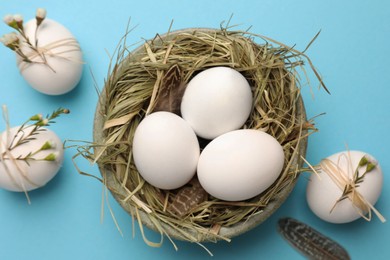 Nest with chicken eggs and natural decor on light blue background, flat lay. Happy Easter