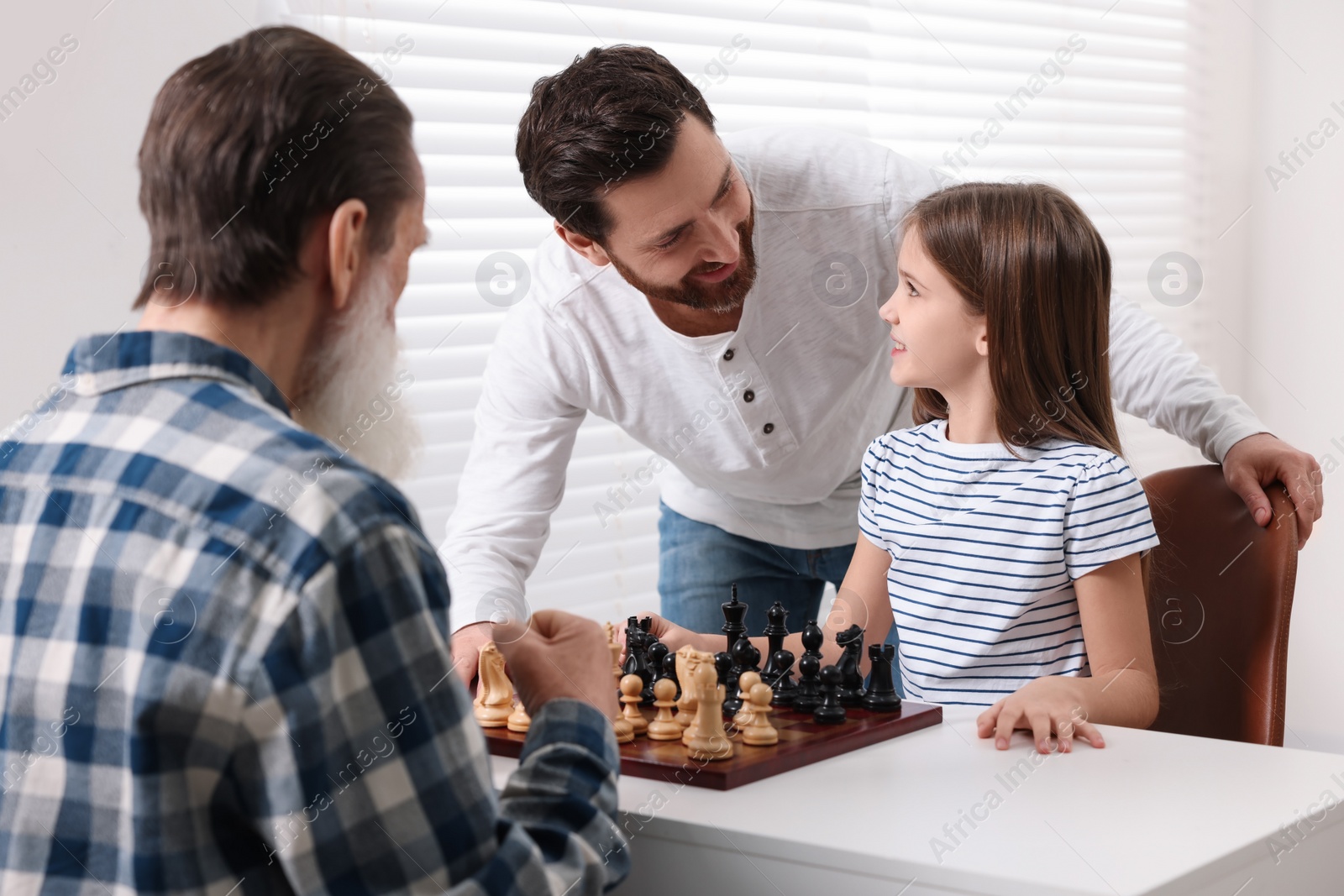 Photo of Family playing chess together at table in room