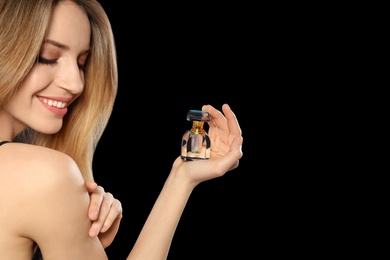 Photo of Young woman with bottle of perfume on black background, closeup
