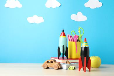Bright toy rockets, car and school supplies on wooden table. Space for text