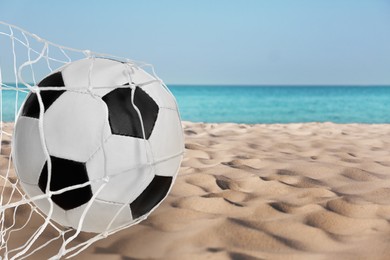 Image of Soccer ball in net on sandy coast near sea. Beach football