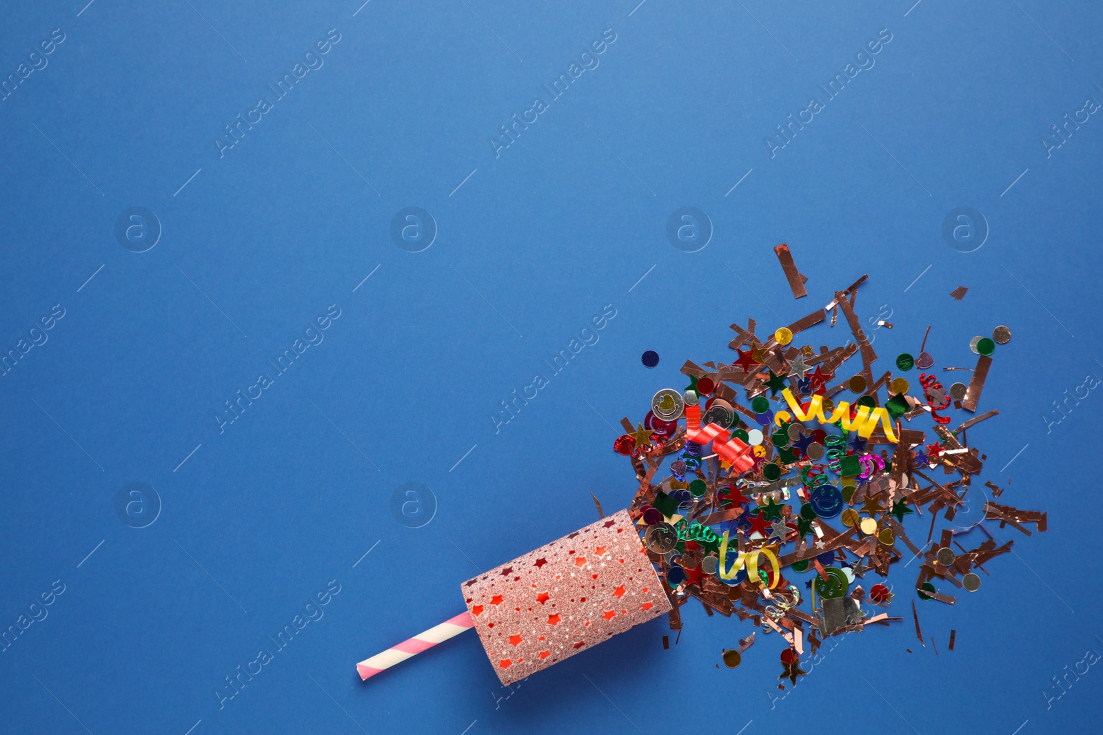 Photo of Confetti and streamers with party cracker on blue background, top view. Space for text