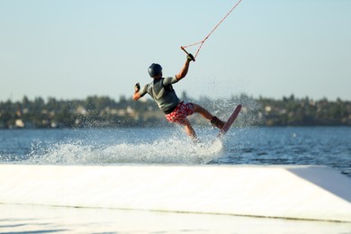 Photo of Teenage wakeboarder doing trick over river, back view. Extreme water sport