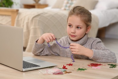 Photo of Little girl learning to make beaded jewelry with online course at home. Time for hobby