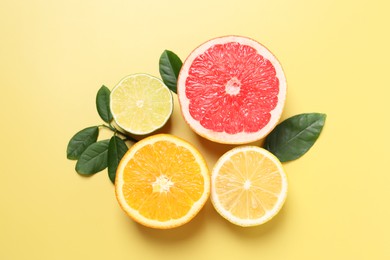 Photo of Different cut citrus fruits and leaves on yellow table, flat lay