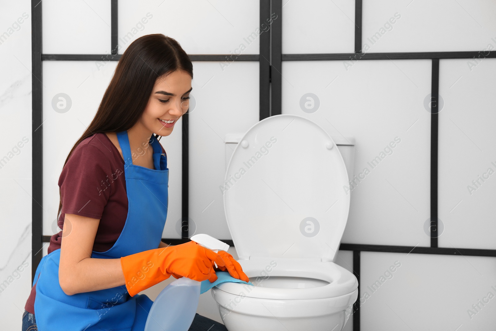 Photo of Young woman cleaning toilet bowl in bathroom