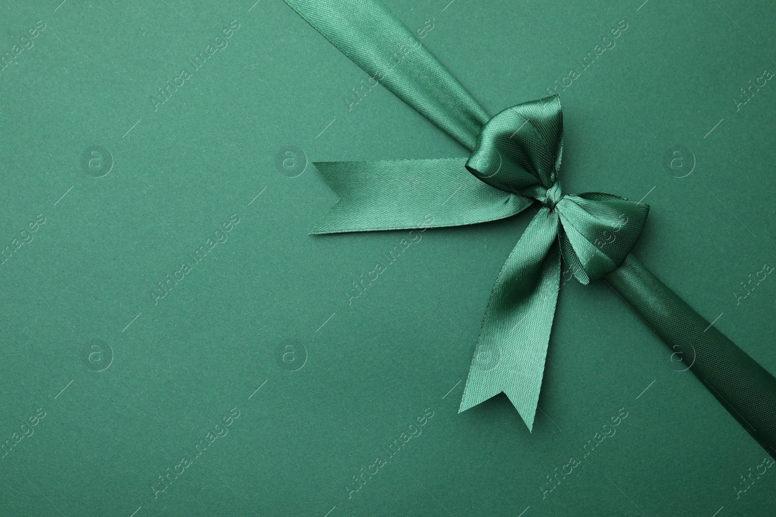 Photo of Bright satin ribbon with bow on green background, top view. Space for text