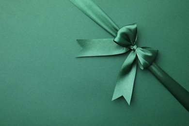 Photo of Bright satin ribbon with bow on green background, top view. Space for text