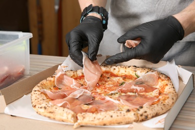 Professional chef adding prosciutto to Italian oven baked pizza in restaurant, closeup