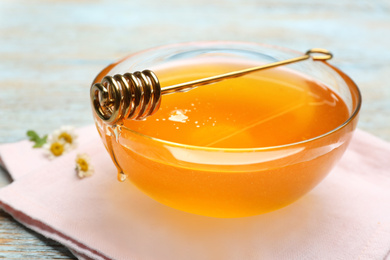 Photo of Tasty honey in glass bowl on wooden table, closeup