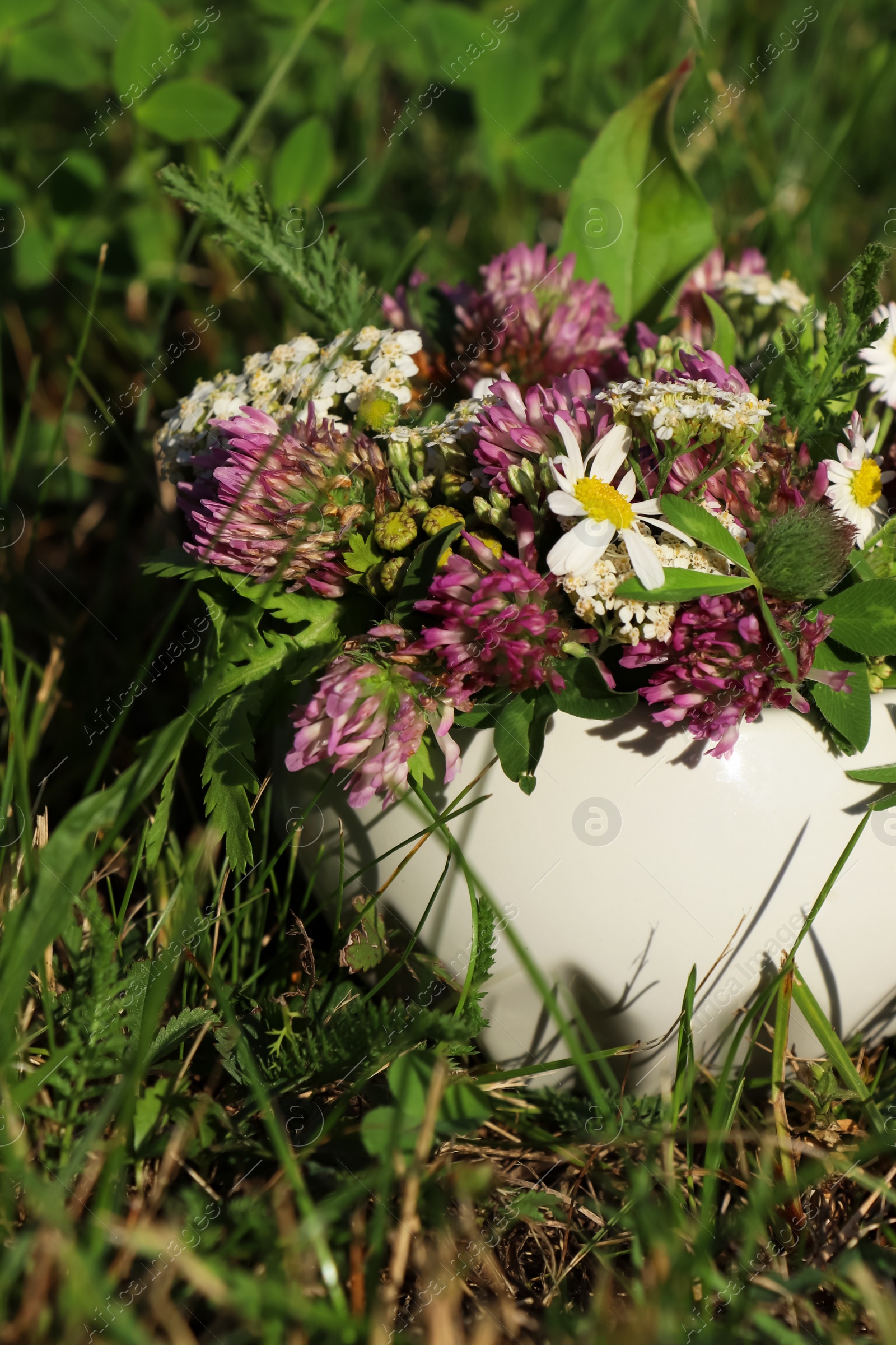Photo of Ceramic mortar with different wildflowers and herbs on green grass outdoors, closeup