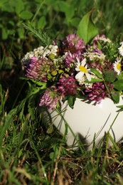 Ceramic mortar with different wildflowers and herbs on green grass outdoors, closeup