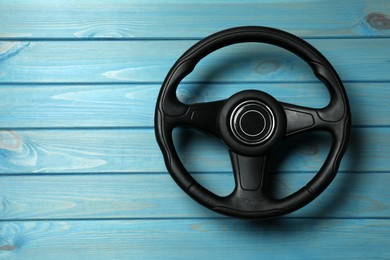 New black steering wheel on light blue wooden table, top view. Space for text