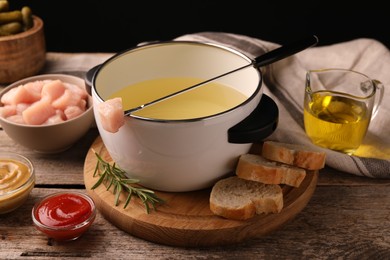 Fondue pot with oil, fork, raw meat pieces and other products on wooden table