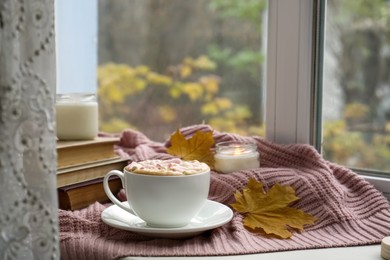 Cup of tasty hot drink with marshmallows near books, leaves and burning candle on blanket, space for text. Autumn coziness