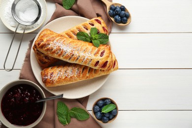 Fresh tasty puff pastry with sugar powder, blueberries and mint served on white wooden table, flat lay. Space for text