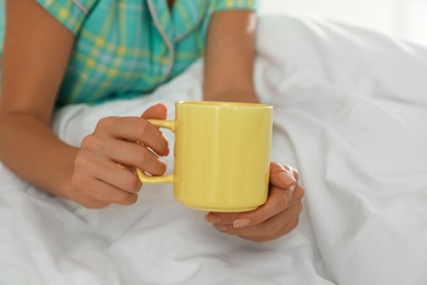 Photo of Woman with yellow cup in bed at home, closeup