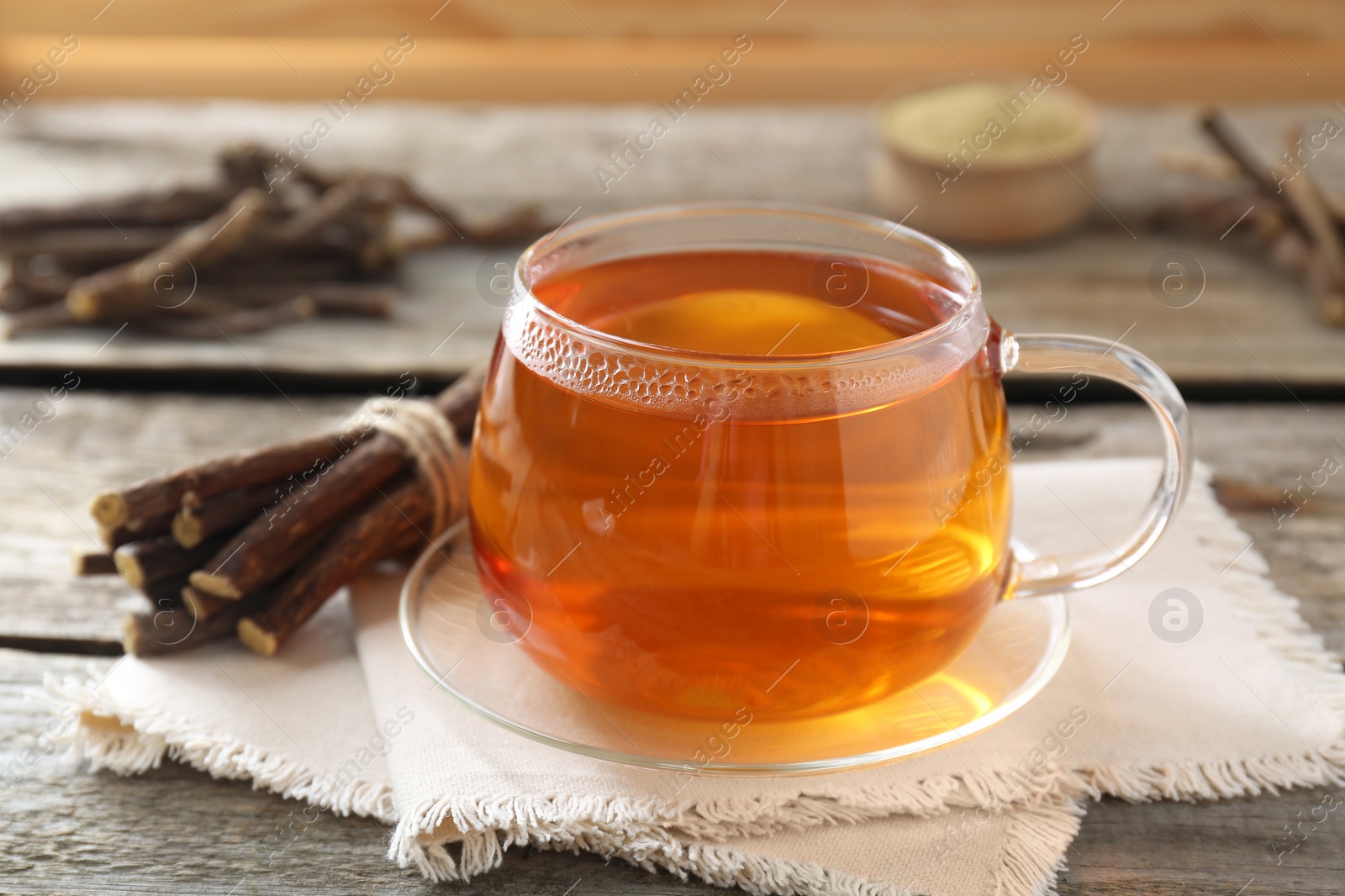 Photo of Aromatic licorice tea in cup and dried sticks of licorice root on wooden table