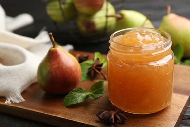 Photo of Delicious pear jam and fresh fruit on black wooden table, closeup
