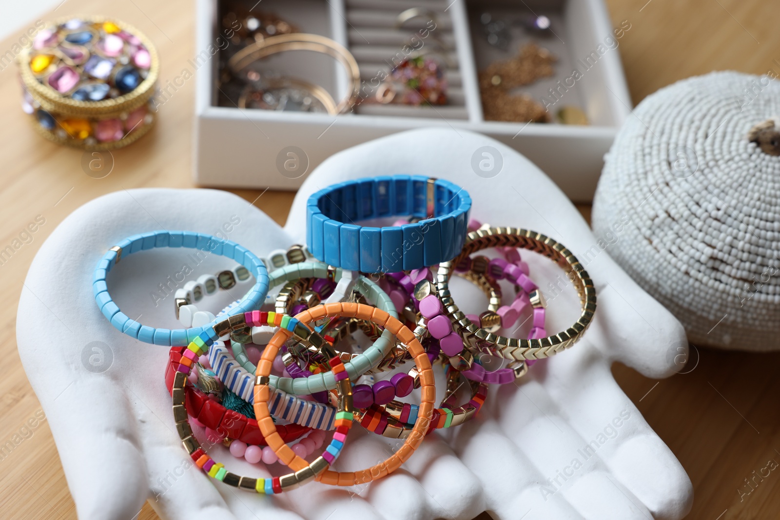 Photo of Ceramic hand stand with many stylish bracelets and jewelry boxes on wooden table, closeup