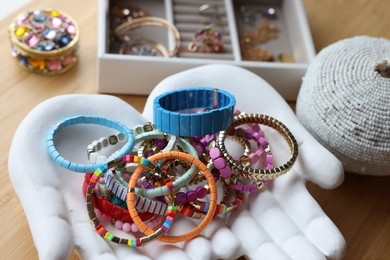 Photo of Ceramic hand stand with many stylish bracelets and jewelry boxes on wooden table, closeup