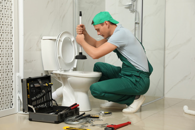 Professional plumber unclogging drain of toilet bowl in bathroom