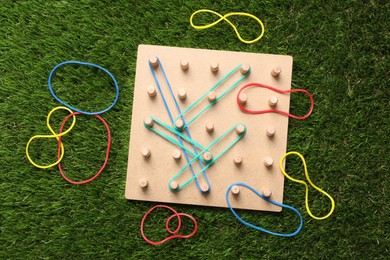 Wooden geoboard with rubber bands on artificial grass, flat lay. Educational toy for motor skills development