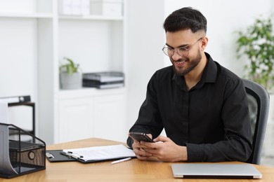 Handsome young man using smartphone at wooden table in office