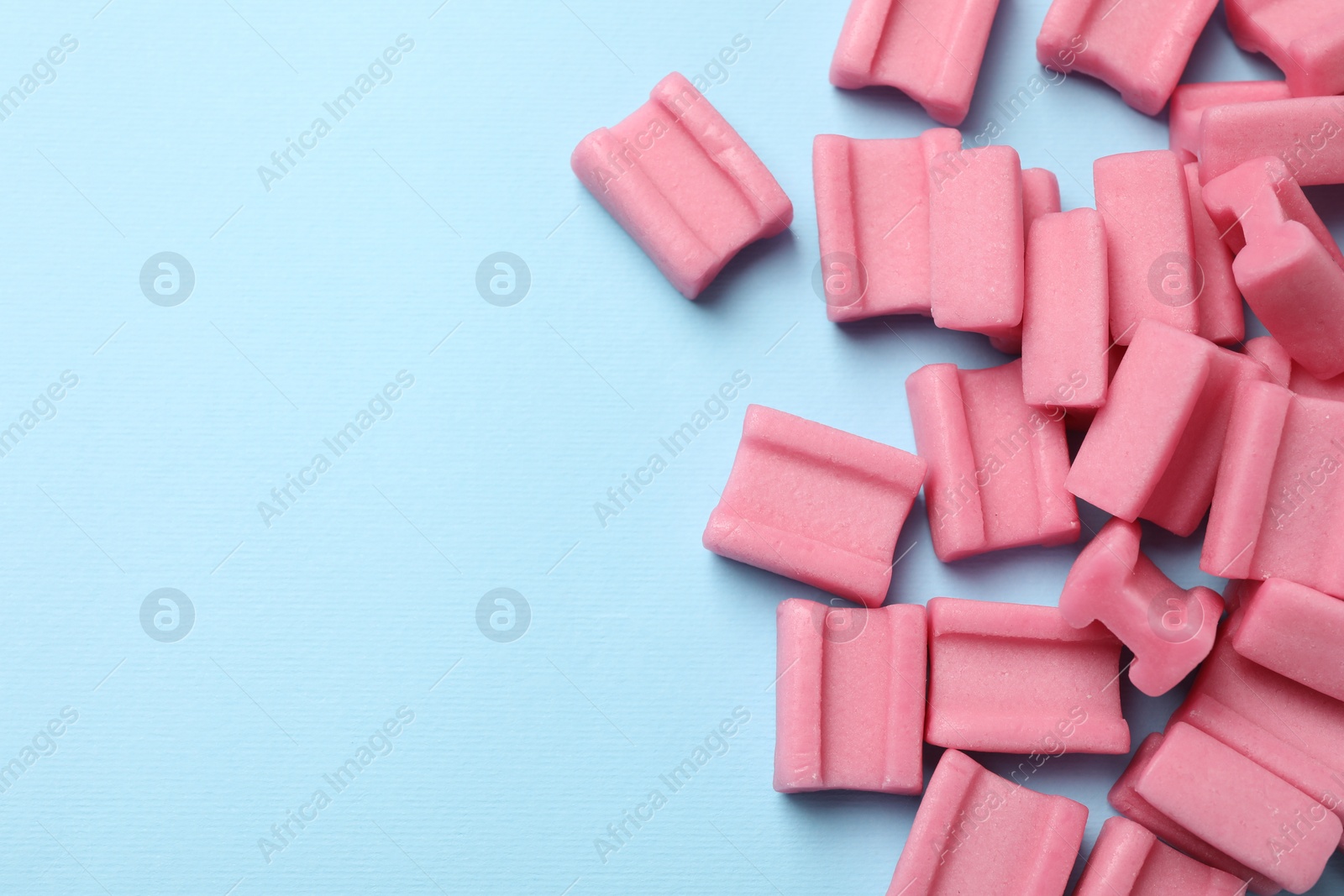 Photo of Tasty pink chewing gums on light blue background, flat lay. Space for text