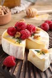 Photo of Brie cheese served with raspberries, walnuts and honey on table, closeup