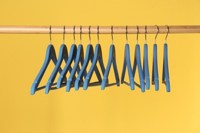 Wooden rack with clothes hangers on color background