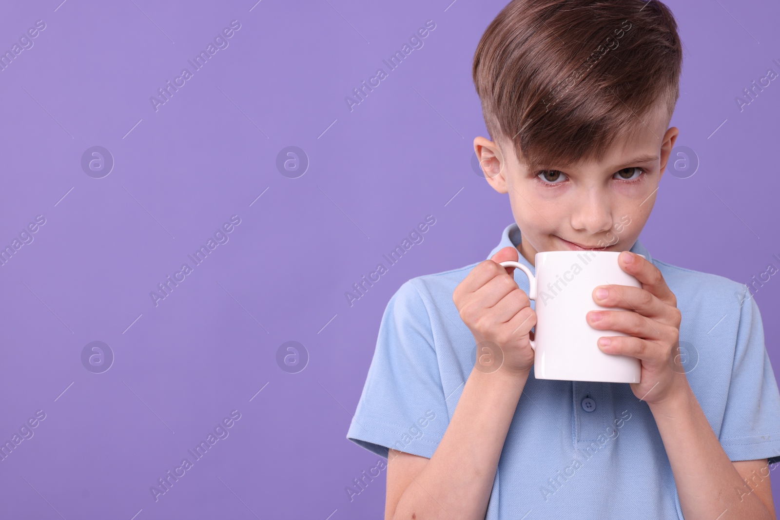 Photo of Cute boy drinking from white ceramic mug on violet background, space for text