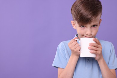 Photo of Cute boy drinking from white ceramic mug on violet background, space for text