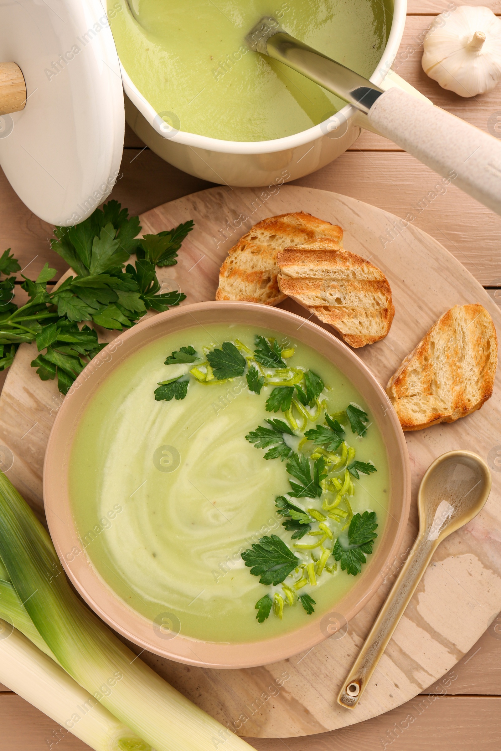 Photo of Delicious leek soup served on beige wooden table, flat lay